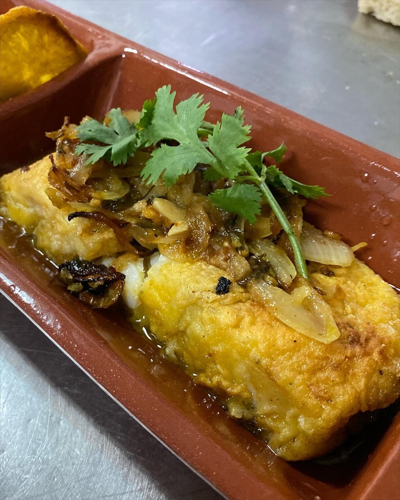 Bacalhau numa travessa de barro, com cebola e coentros por cima