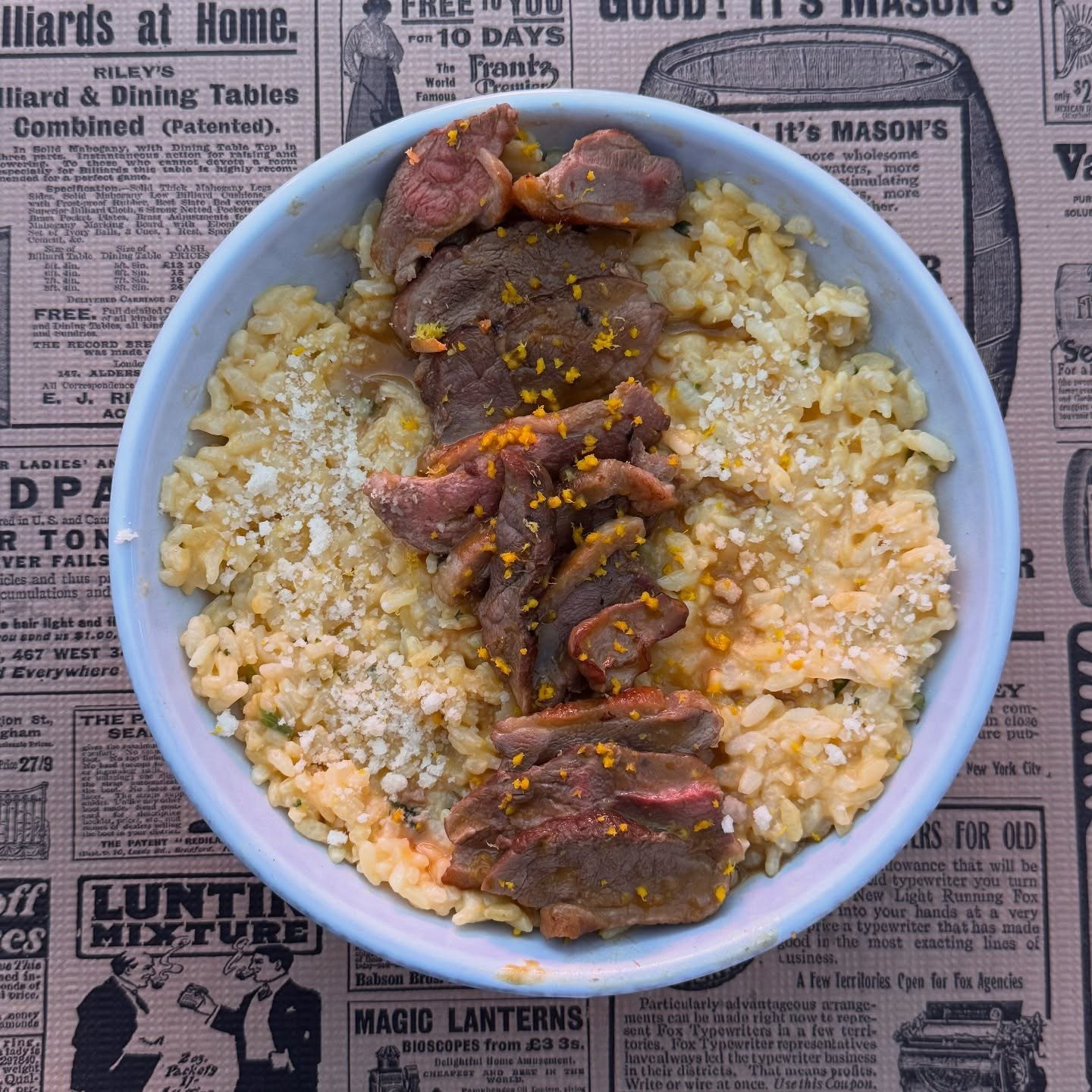 Risoto num prato azul com fatias de peito de pato e raspa de laranja