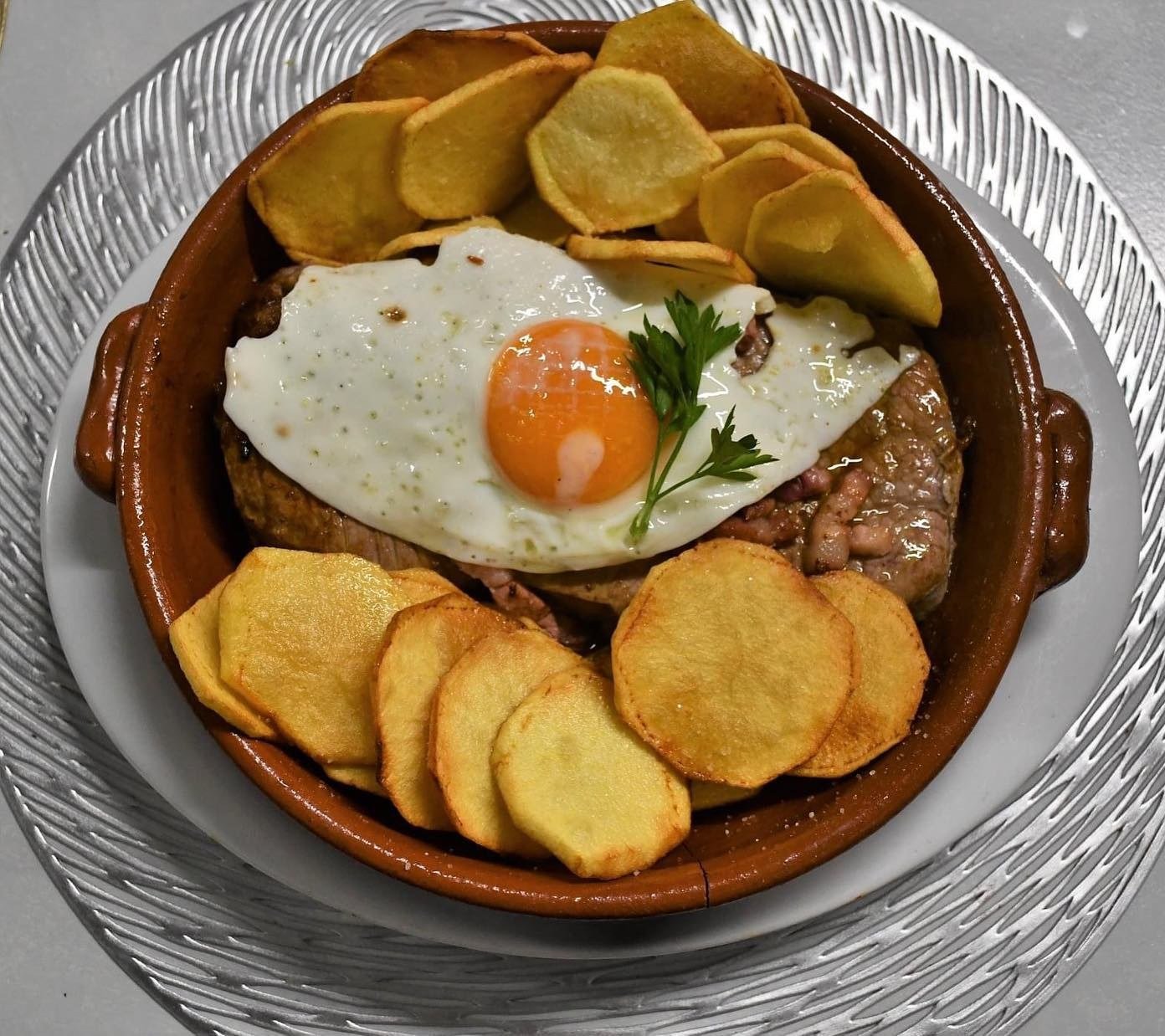 Bife num tacho de barro com ovo estrelado e batatas fritas às rodelas