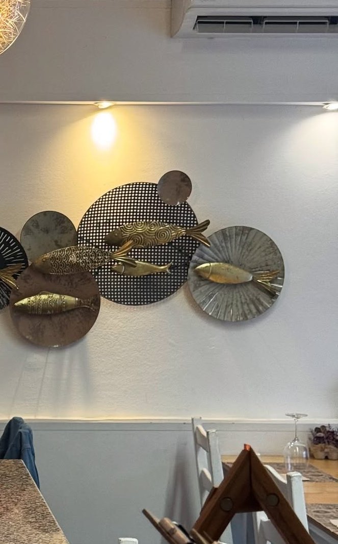 Parede branca da sala decorada com peixes dourados em discos de metal, com cadeiras brancas em baixo