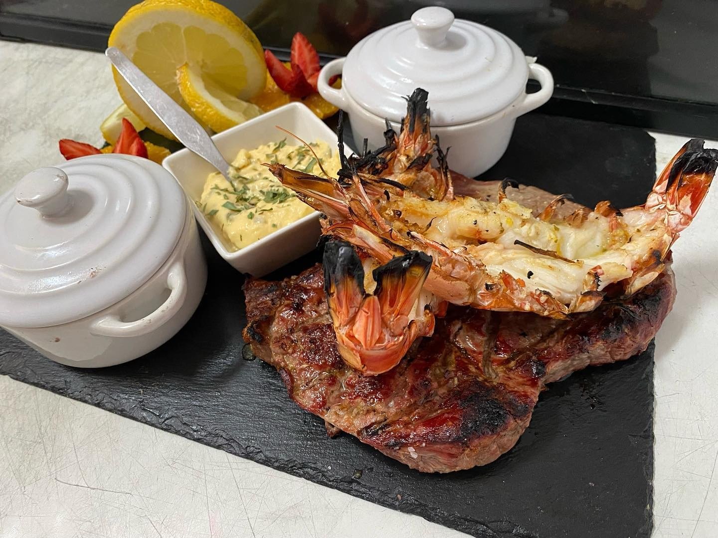 Bife grelhado com marisco grelhado aberto ao meio, servido numa ardósia com limão e molho