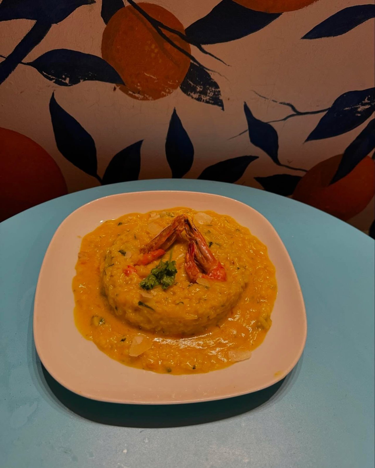 Risoto de camarão num prato raso, sobre toalha com laranjas desenhadas
